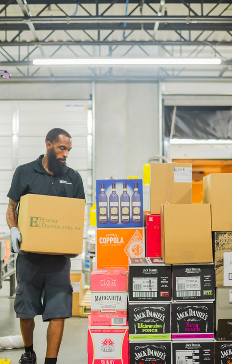Home_NCBeerandWine_FairMarket Employee walking at the warehouse holding a case of wine