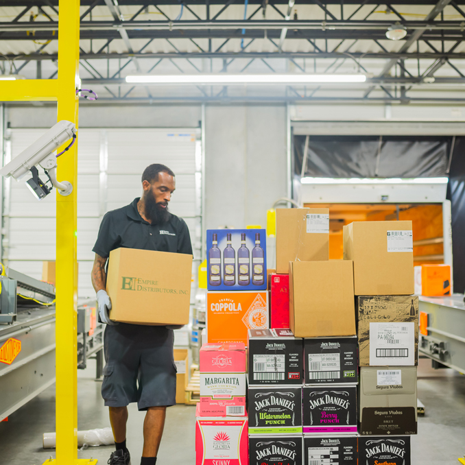 Home_NCBeerandWine_FairMarket_Mobile Employee walking at the warehouse holding a case of wine